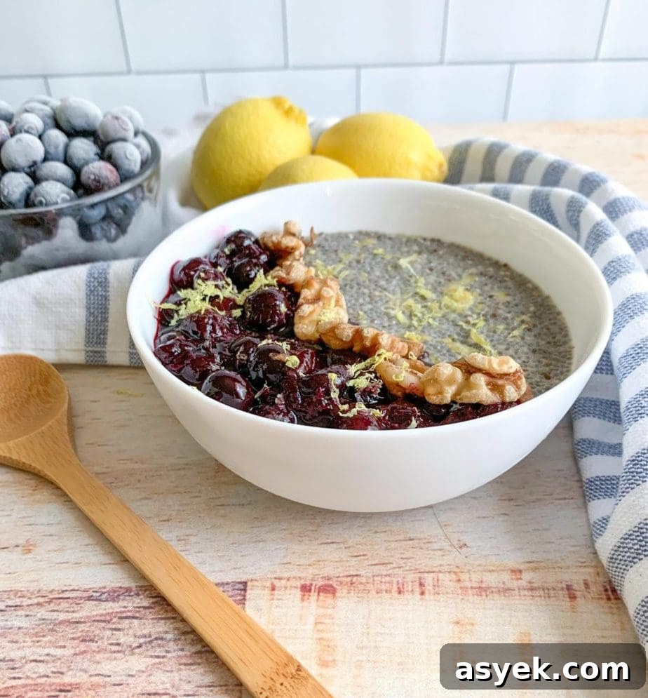 Chia pudding with blueberry jam and walnuts in a white bowl. Blueberries, lemons and a wooden spoon sit alongside.