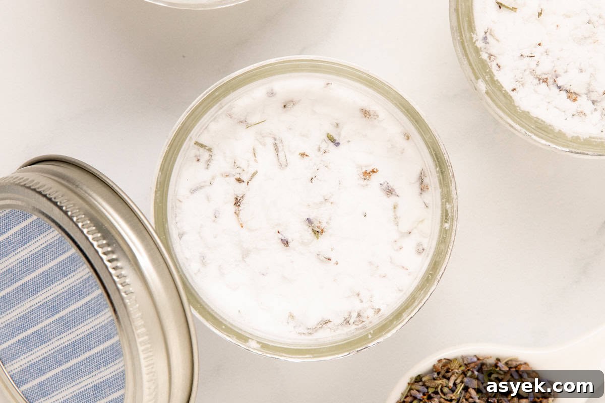 mason jars of homemade air freshener with a bottle of lavender essential oil and a spoonful of lavender buds next to it