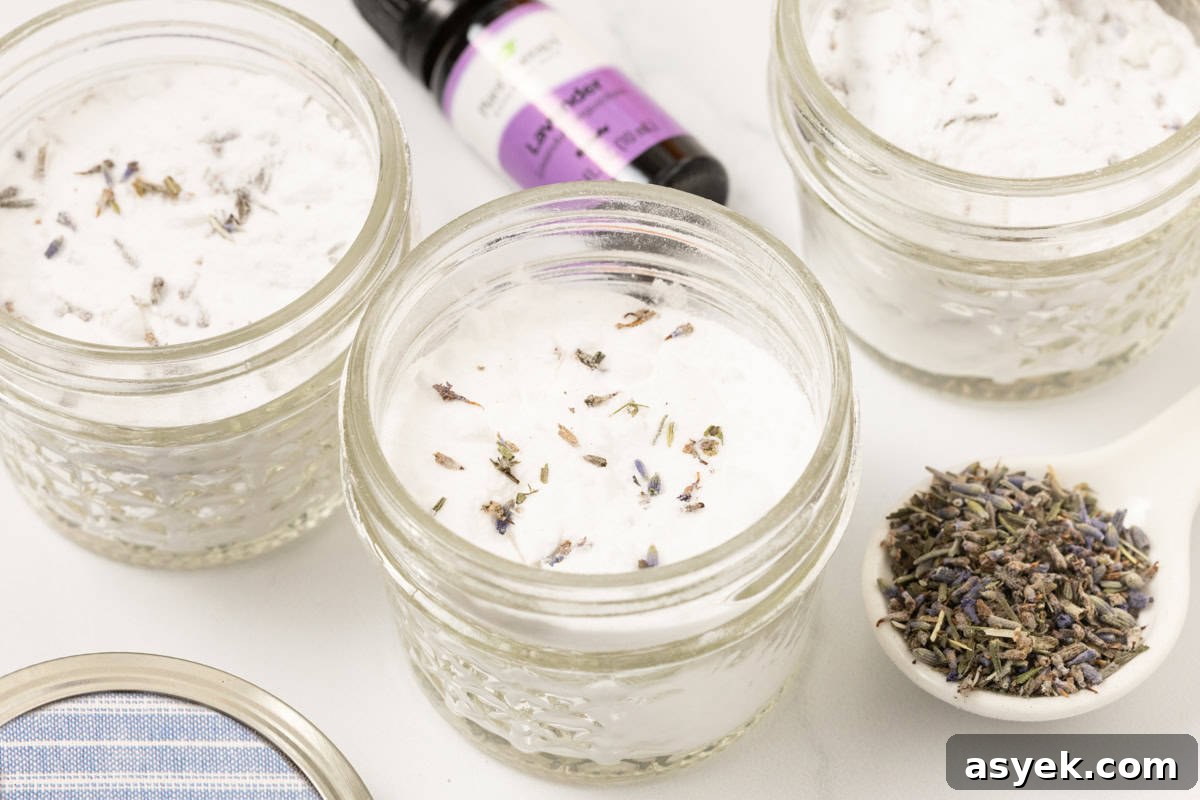 mason jars of homemade air freshener with a bottle of lavender essential oil and a spoonful of lavender buds next to it