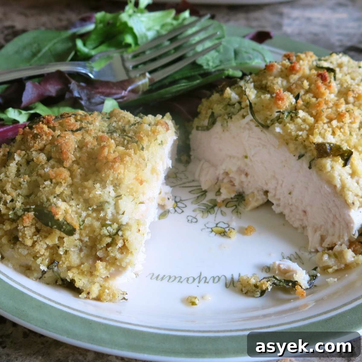 Crispy Parmesan Herb-Crusted Chicken Recipe 6 Baked herb crusted chicken breast cut in half to expose juicy center on a plate.