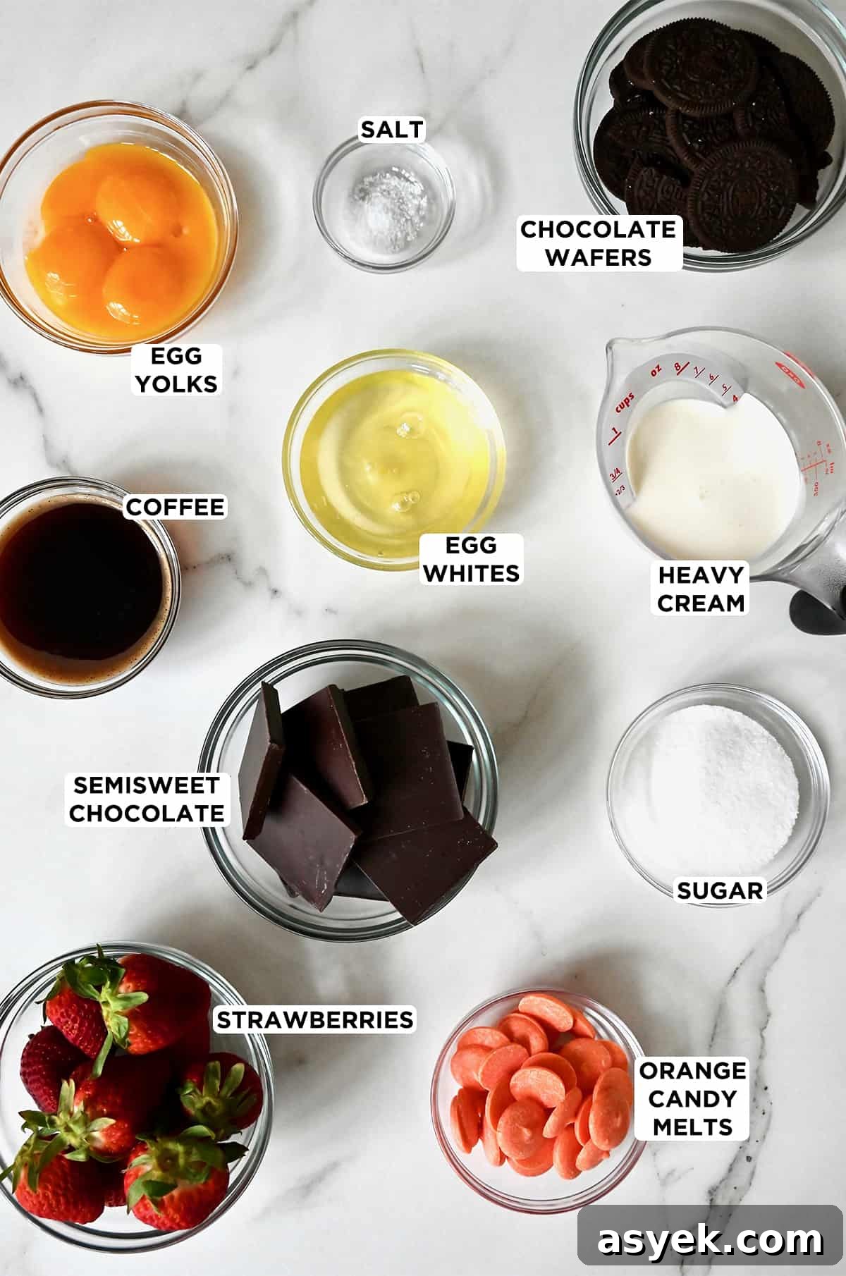 Small glass bowls of strawberries, orange candy melts, sugar, chocolate, coffee, egg whites, heavy cream, chocolate wafers, egg whites and yolks, and salt.