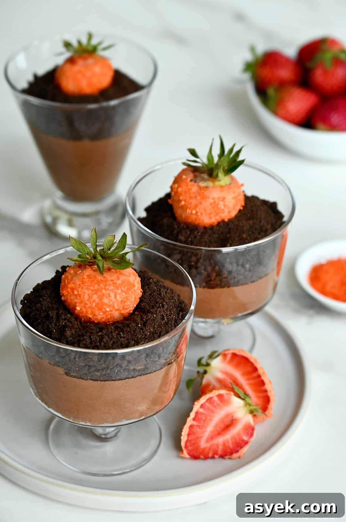 Three chocolate mousse parfaits topped with crushed chocolate wafers and strawberries dipped in orange candy melts.