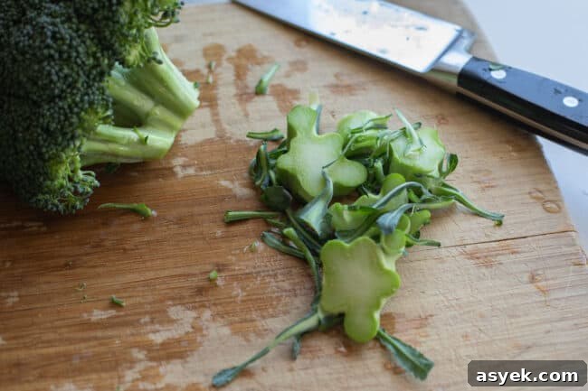 peeling leaves off of broccoli stems, chopping of end of broccoli stems on a wooden cutting board.