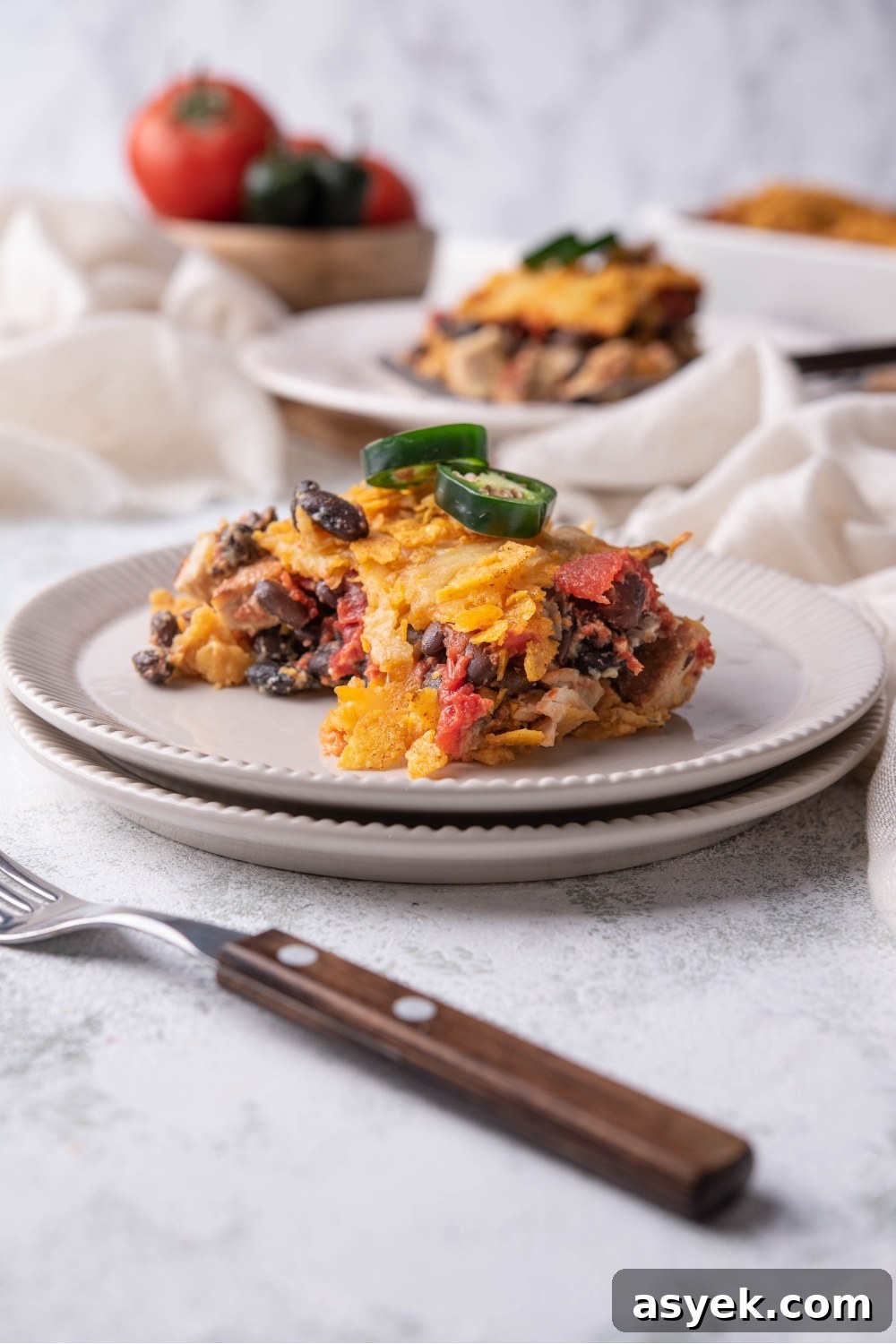 Mexican Chicken Casserole Recipe with Cheesy Tortilla Topping 2 Serving of Mexican chicken casserole on a white plate garnished with fresh jalapeños and a fork next to the plate.