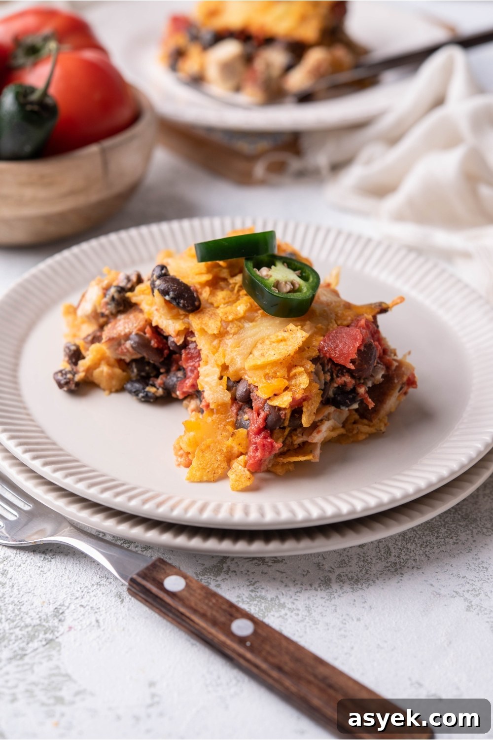 Mexican Chicken Casserole Recipe with Cheesy Tortilla Topping 8 Serving of Mexican chicken casserole on a white plate garnished with fresh jalapeños and a fork next to the plate.