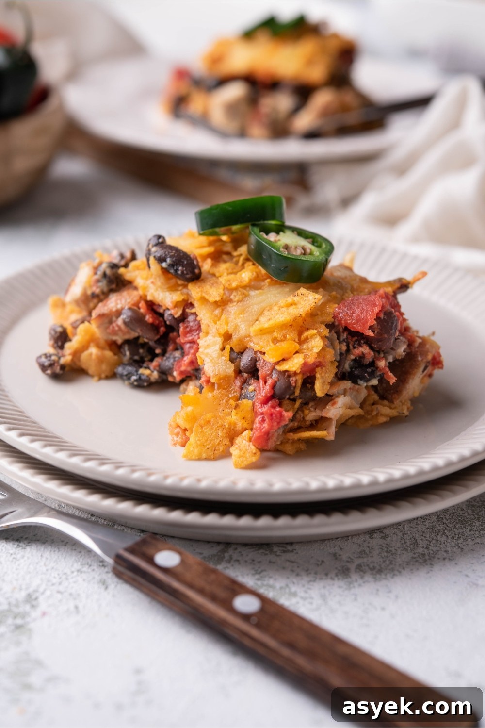 Mexican Chicken Casserole Recipe with Cheesy Tortilla Topping 9 Serving of Mexican chicken casserole on a white plate garnished with fresh jalapeños and a fork next to the plate.
