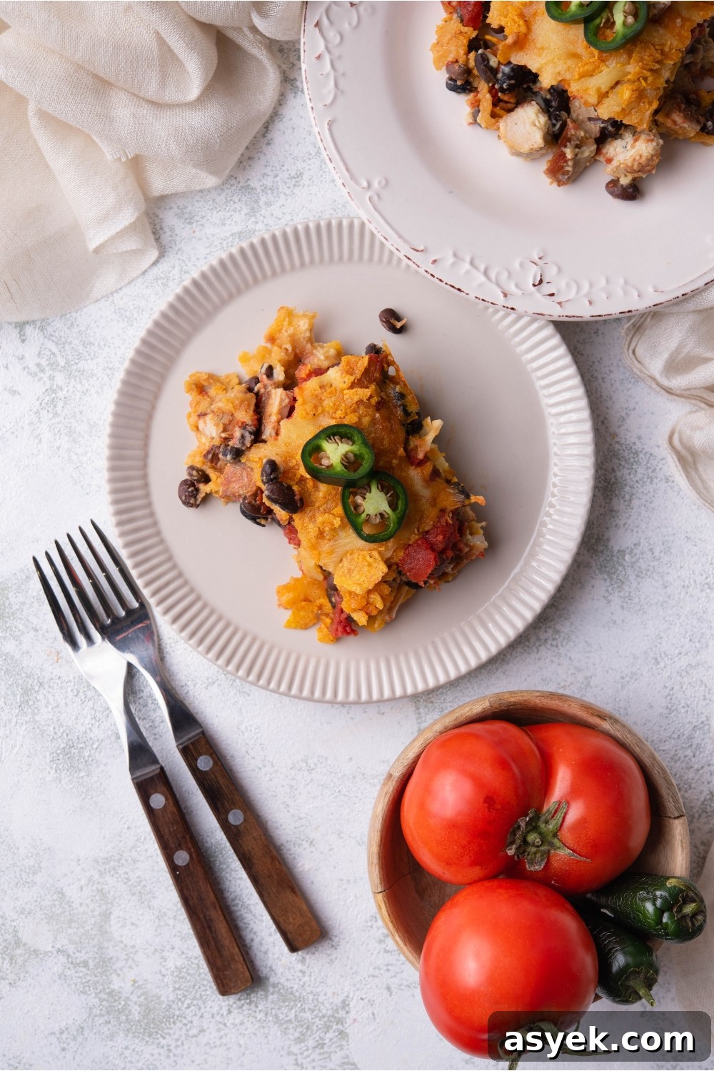 Mexican Chicken Casserole Recipe with Cheesy Tortilla Topping 3 Overview of a serving of Mexican chicken casserole on a white plate next to two forks and a second serving of casserole.