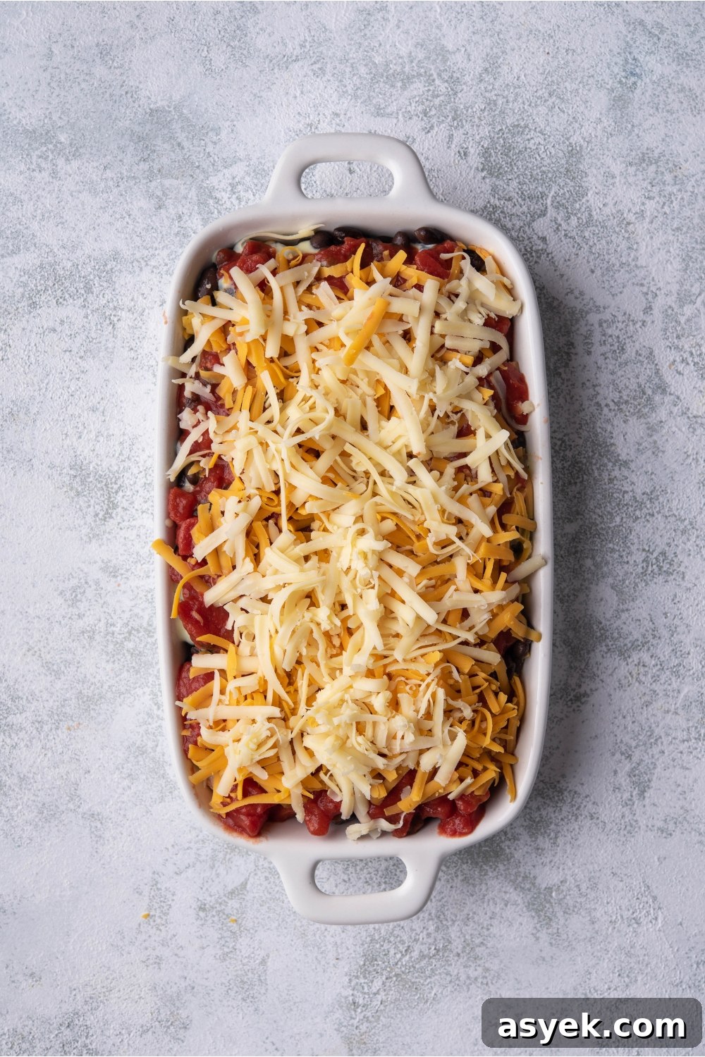 Mexican Chicken Casserole Recipe with Cheesy Tortilla Topping 6 White baking dish with unbaked Mexican chicken casserole.