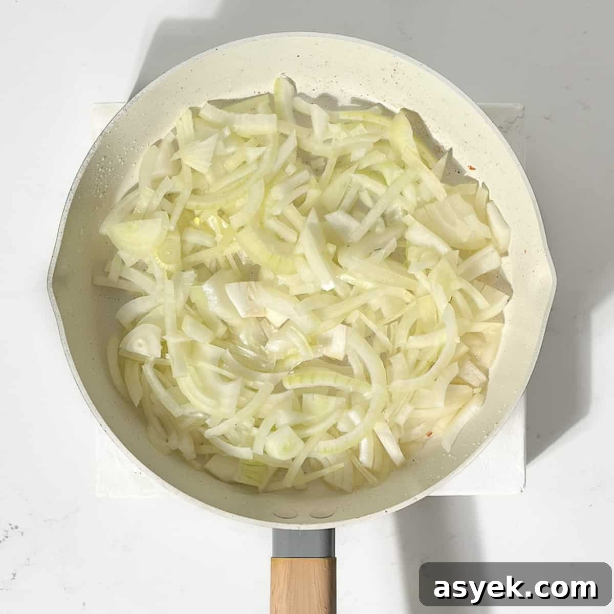 Sliced onions frying in a large frying pan.