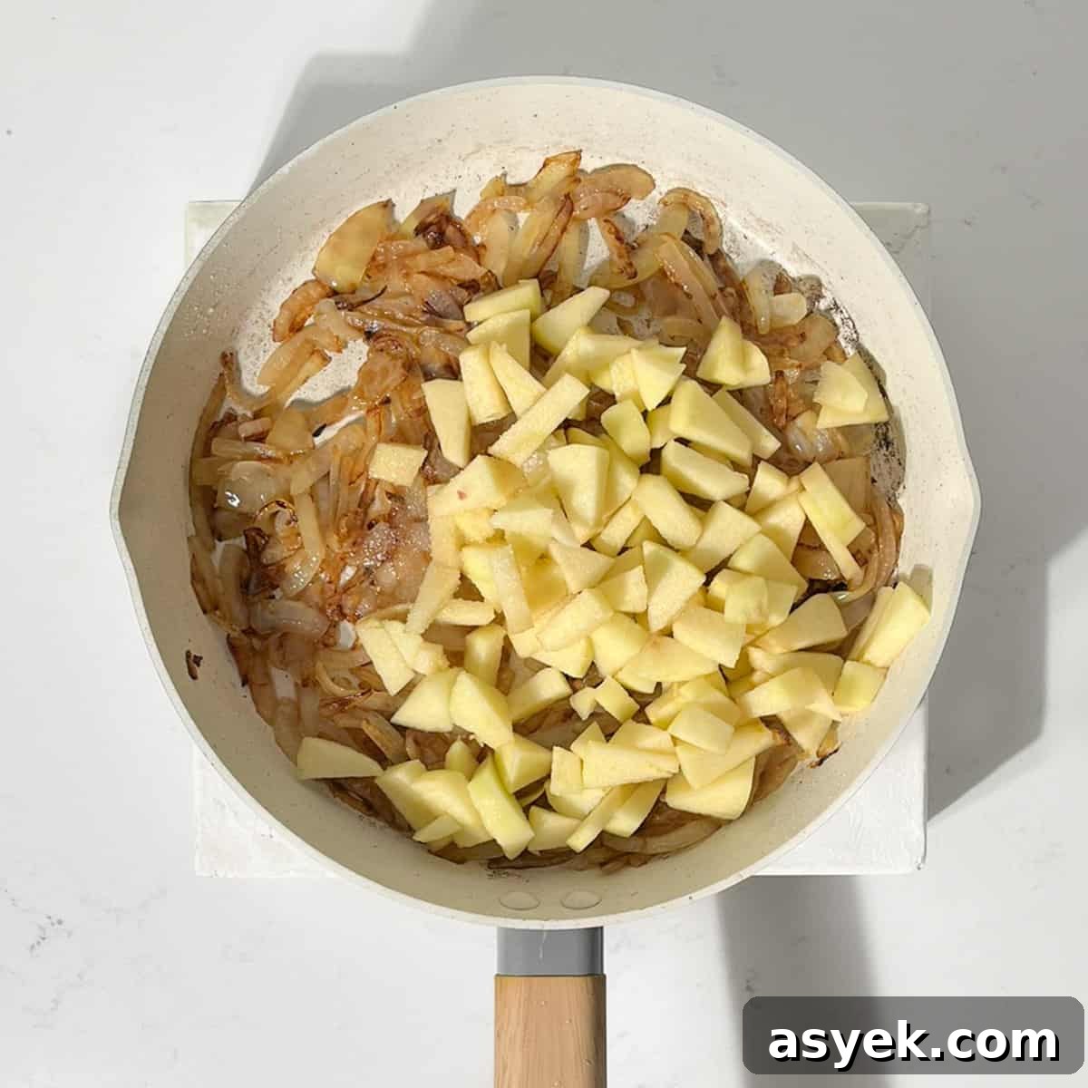 Apples and onions cooking in a frying pan.
