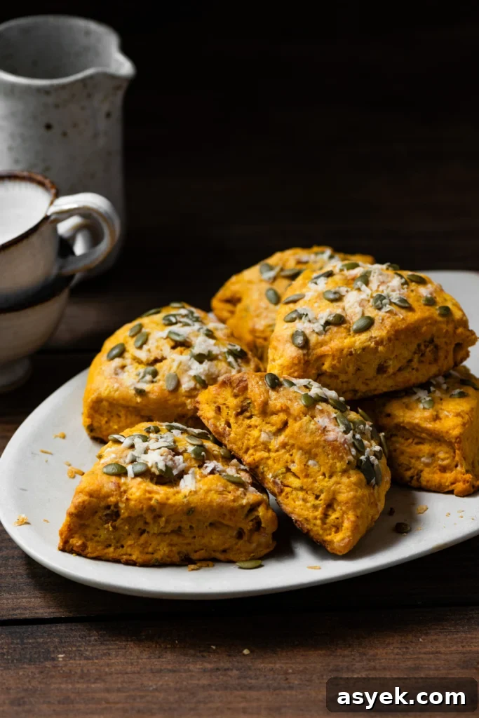 Savory Pumpkin Cheddar Scones 3 pumpkin scones topped with cheese and pepita seeds stacked on a plate.