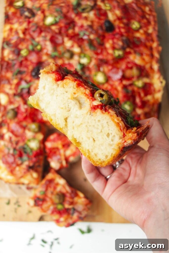 Pepperoni Focaccia Pizza Bread with Crispy Cheese Crust 15 Side view of a hand holding up focaccia pizza, with the rest of the pizza in the background.