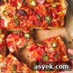 Hand pulling out a piece of focaccia pizza from the rest of the pizza on a large wooden board.