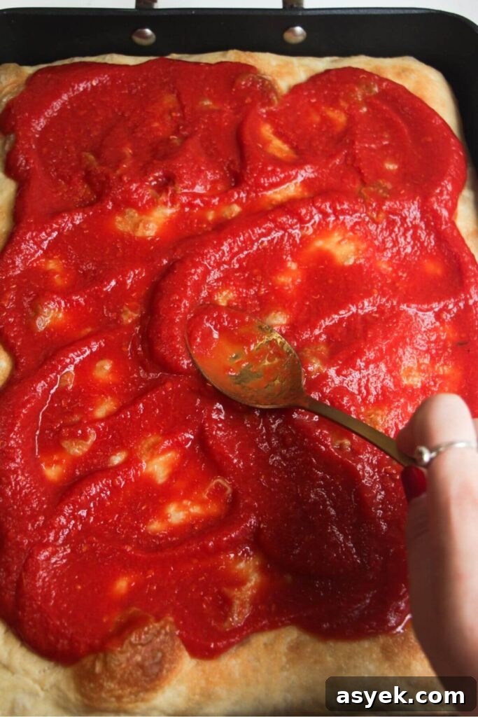 Pepperoni Focaccia Pizza Bread with Crispy Cheese Crust 10 Spreading pizza sauce on top of par-baked focaccia in a large pan.