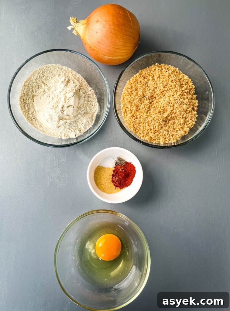 raw onion, crushed pork rinds, flour, raw egg, and seasoning on a flat surface