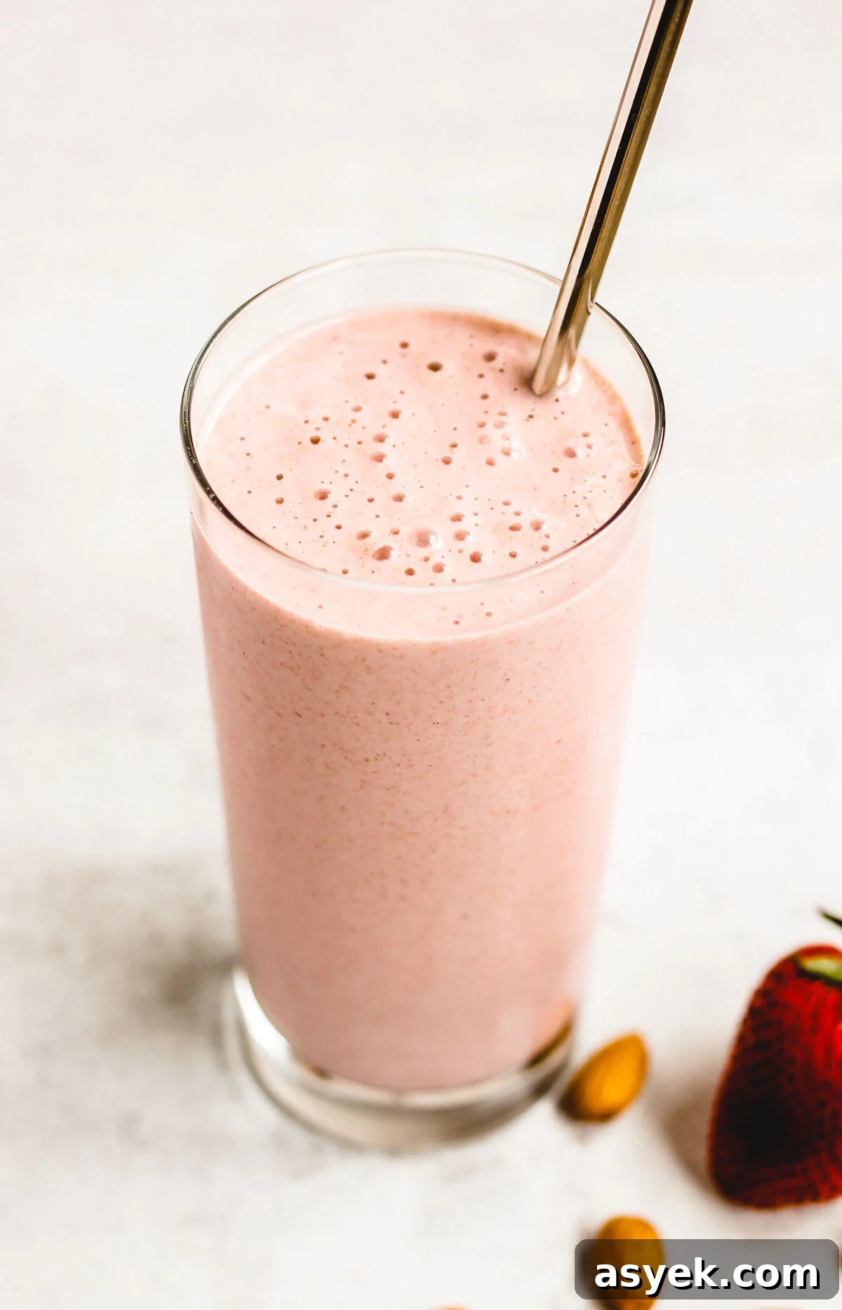 Creamy Dairy-Free Strawberry Almond Smoothie Recipe 4 side angle view of strawberry almond smoothie in a glass with a stainless steel straw