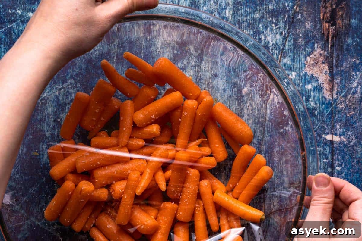 bowl of baby carrots with plastic wrap being applied overtop