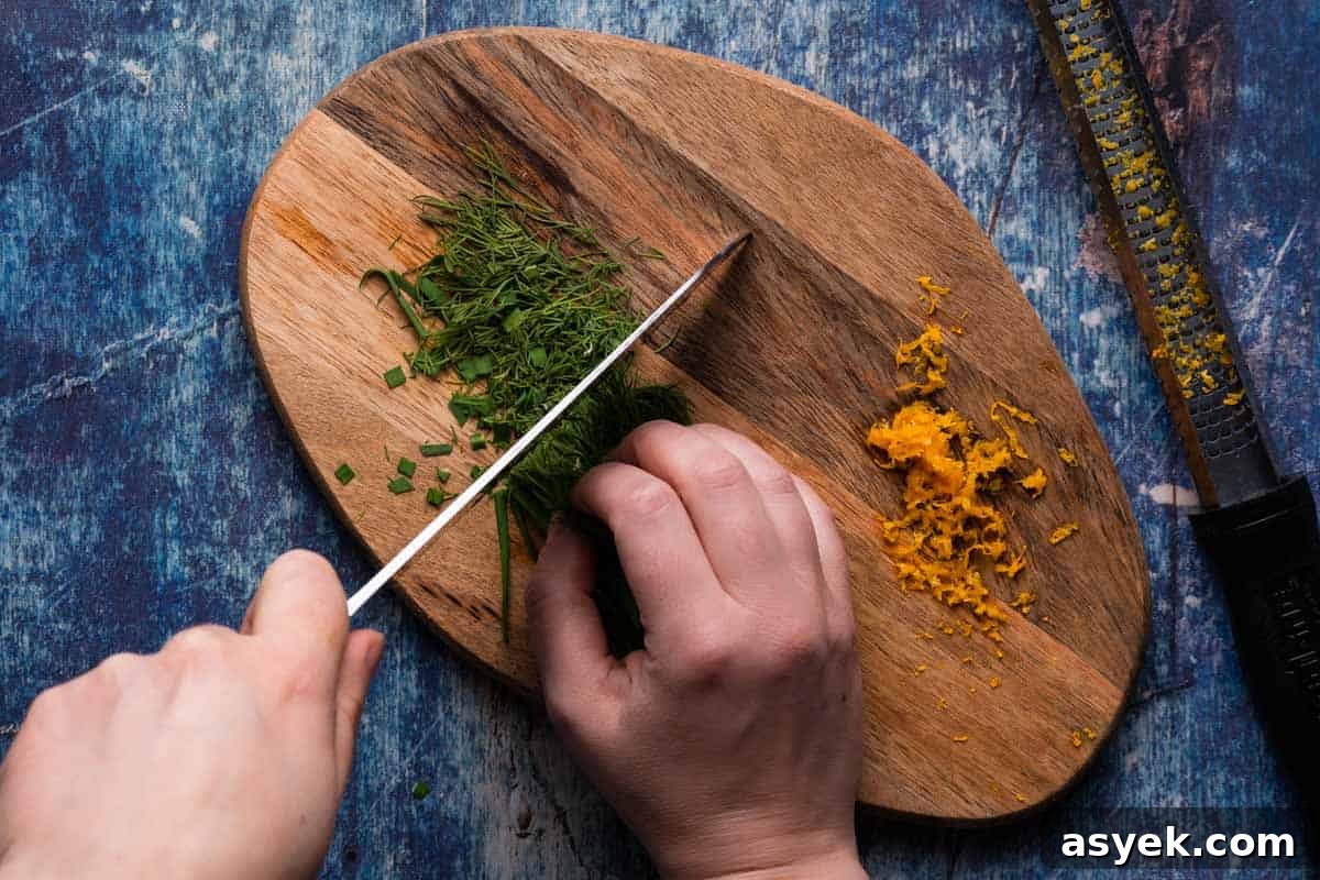 herbs being chopped on wooden cutting board with orange zest on the side