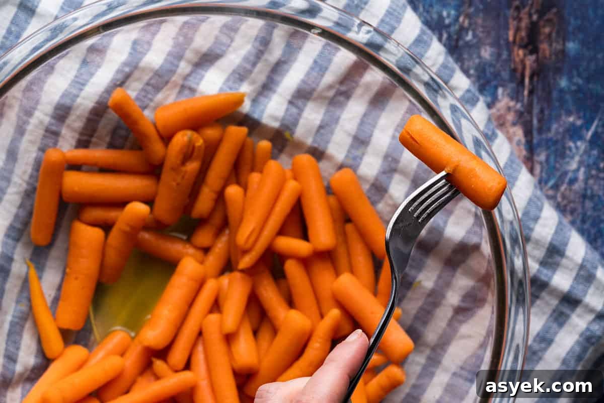 fork piercing cooked baby carrot overtop bowl of carrots