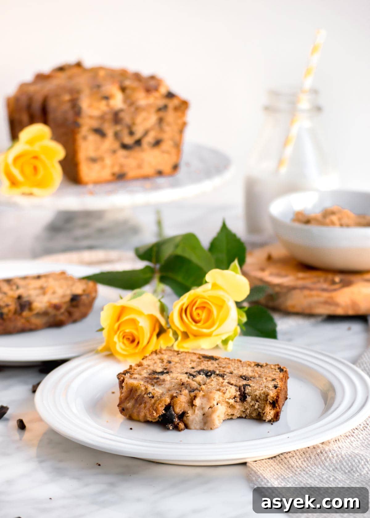 Slice of Chocolate Chip Banana Bread with Walnuts on plate with loaf in background.