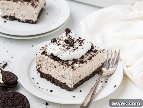 A square slice of no bake oreo cheesecake topped with whipped cream and cookie crumbles.
