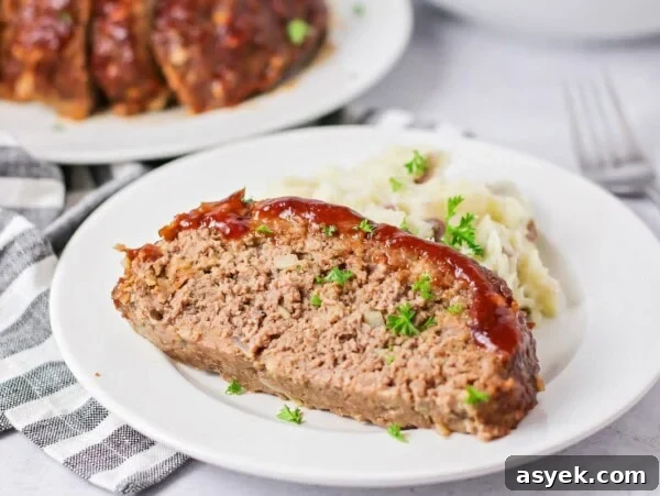 Easy meatloaf recipe slice on white plate with mashed potatoes.