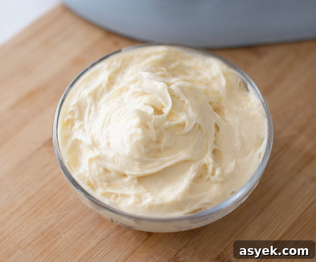 A small glass bowl filled with creamy, smooth butter sits on a wooden surface. The butter is swirled into a fluffy texture, and the wooden surface adds a warm tone to the setup.