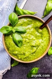 Overhead shot of basil pesto with gold spoon in the bowl and leaves surrounding it.