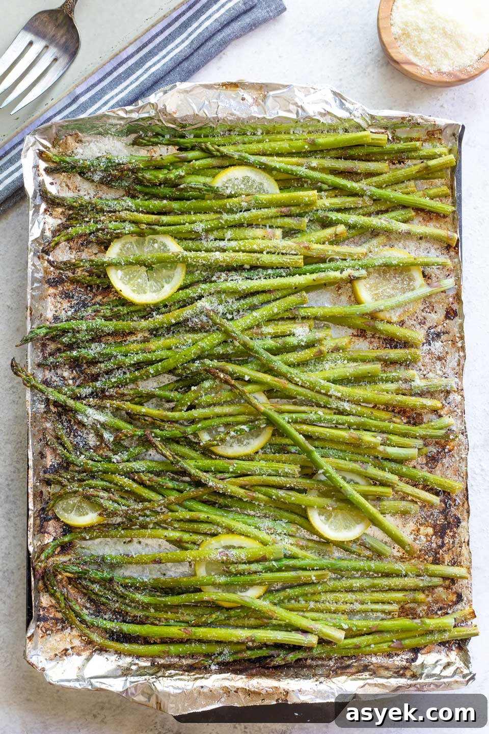 Grilled Asparagus Recipe with Parmesan, Lemon and Garlic 10 Asparagus still on grill pan, sprinkled with parmesan cheese and with lemon slices tucked in.