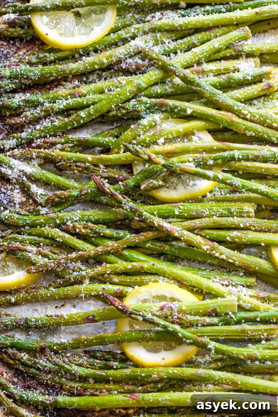 Grilled Asparagus Recipe with Parmesan, Lemon and Garlic 12 Overhead closeup of asparagus and lemon slices sprinkled with parmesan cheese, still on pan after grilling.