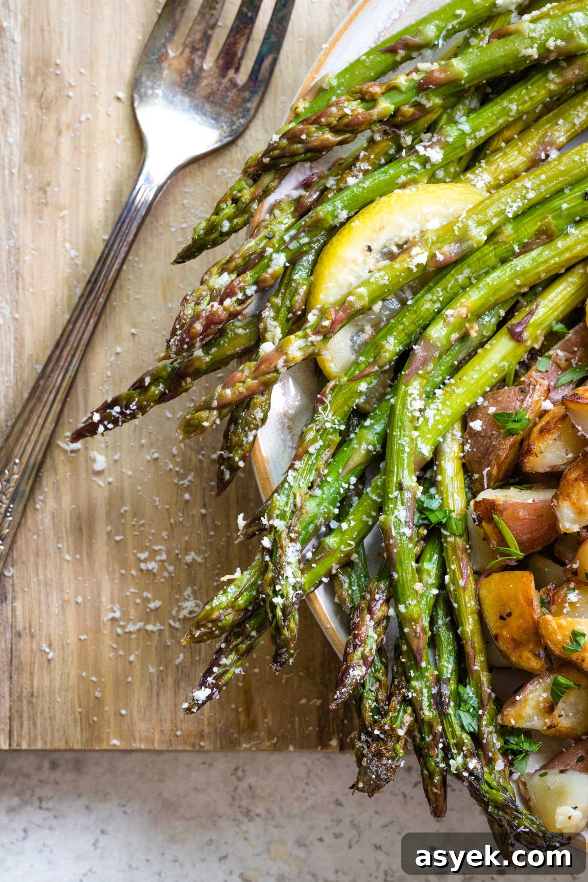 Grilled Asparagus Recipe with Parmesan, Lemon and Garlic 13 Closeup of Asparagus sprinkled with parmesan at edge of dinner plate with potatoes; fork nearby.