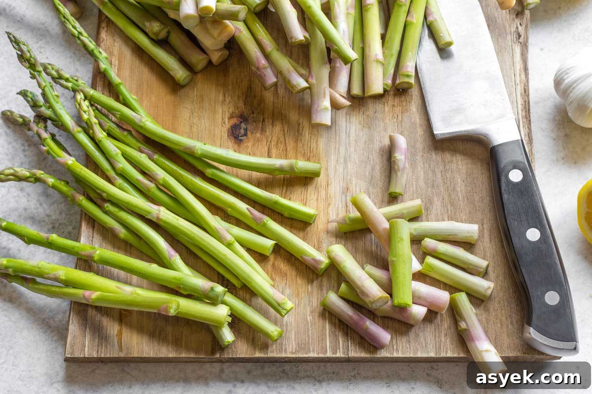 Grilled Asparagus Recipe with Parmesan, Lemon and Garlic 4 Raw asparagus spears on wood cutting board, some with ends trimmed off by knife.