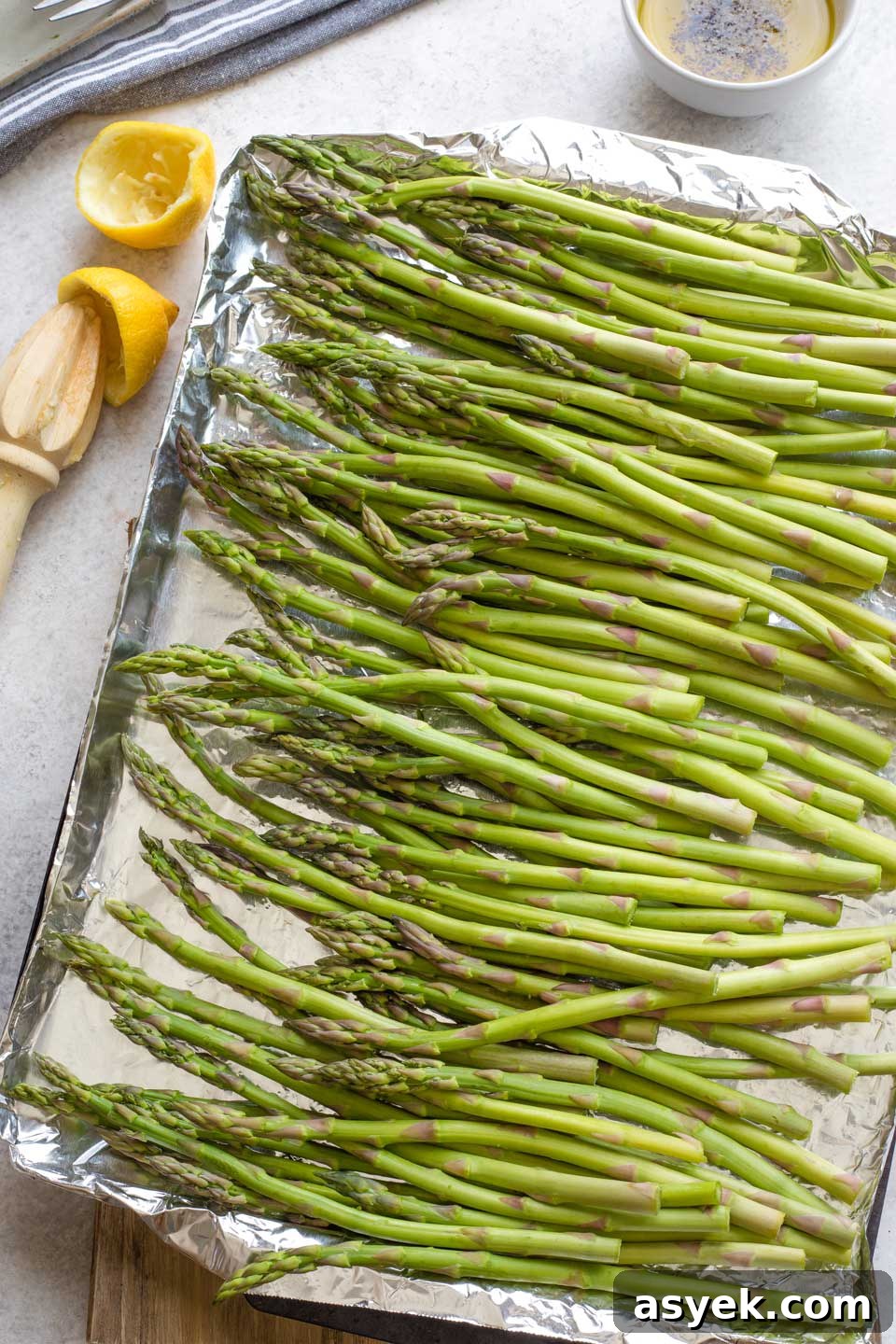 Grilled Asparagus Recipe with Parmesan, Lemon and Garlic 5 Overhead of raw asparagus spread out on heavy duty foil on grill pan; bowl of marinade in background.