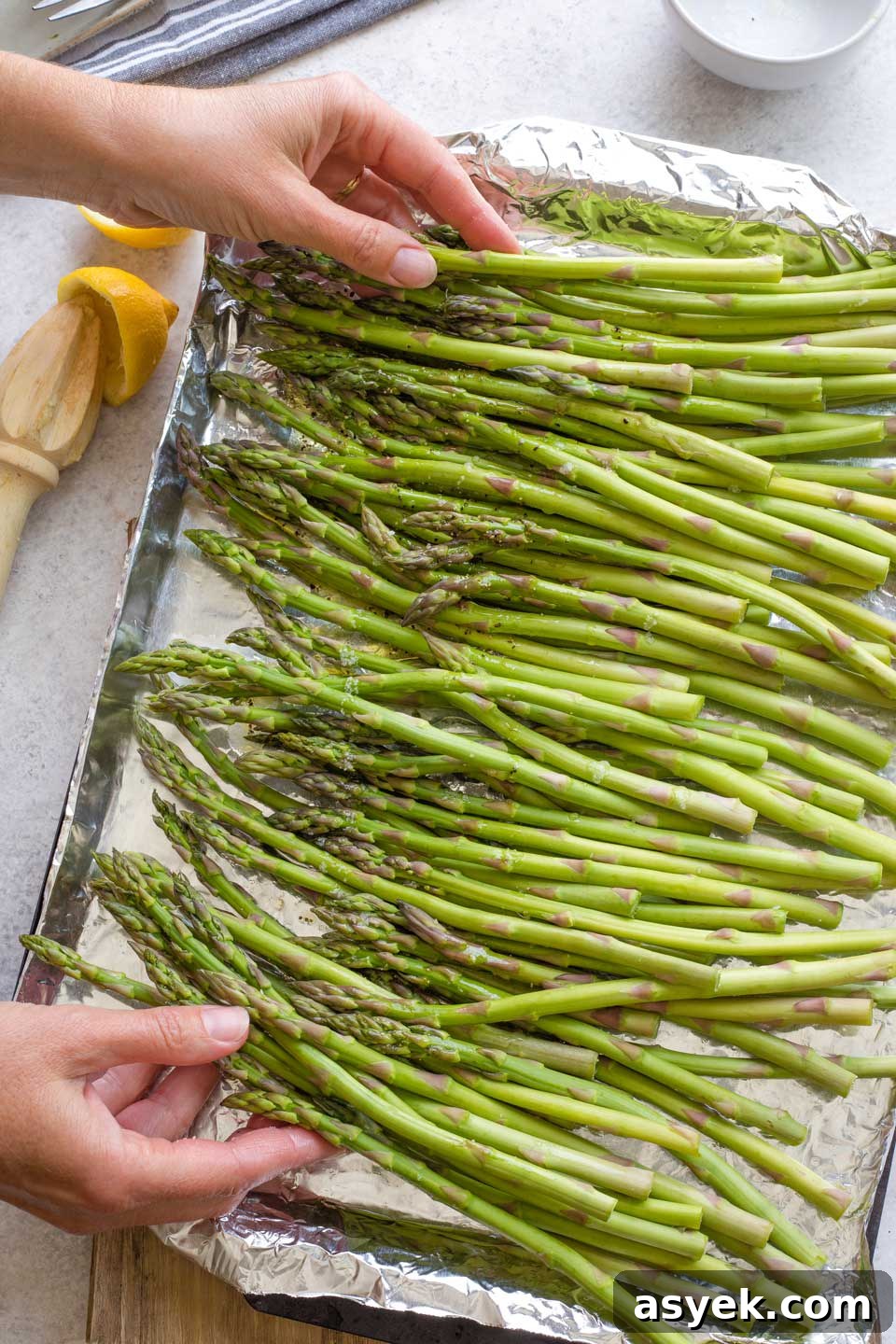 Grilled Asparagus Recipe with Parmesan, Lemon and Garlic 7 Two hands tossing asparagus in lemon and garlic marinade, on foil-lined grill pan.