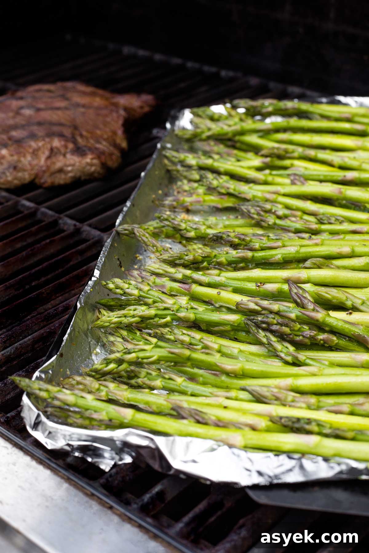 Grilled Asparagus Recipe with Parmesan, Lemon and Garlic 8 Side view of tops of asparagus in pan on grill with steak cooking behind.