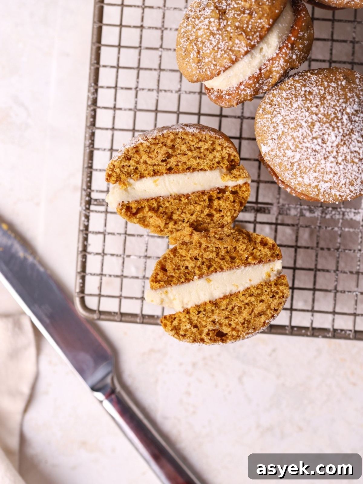 Pumpkin Whoopie Pies with Cream Cheese Filling 5 A pumpkin whoopie pie sliced in half on a wire rack.