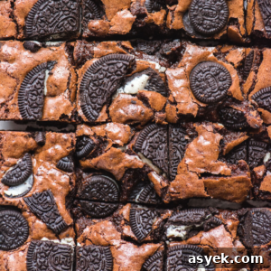Close-up of Oreo brownies topped with pieces of chocolate sandwich cookies, some whole and some broken, creating a rich, textured surface. The brownies are cut into squares.