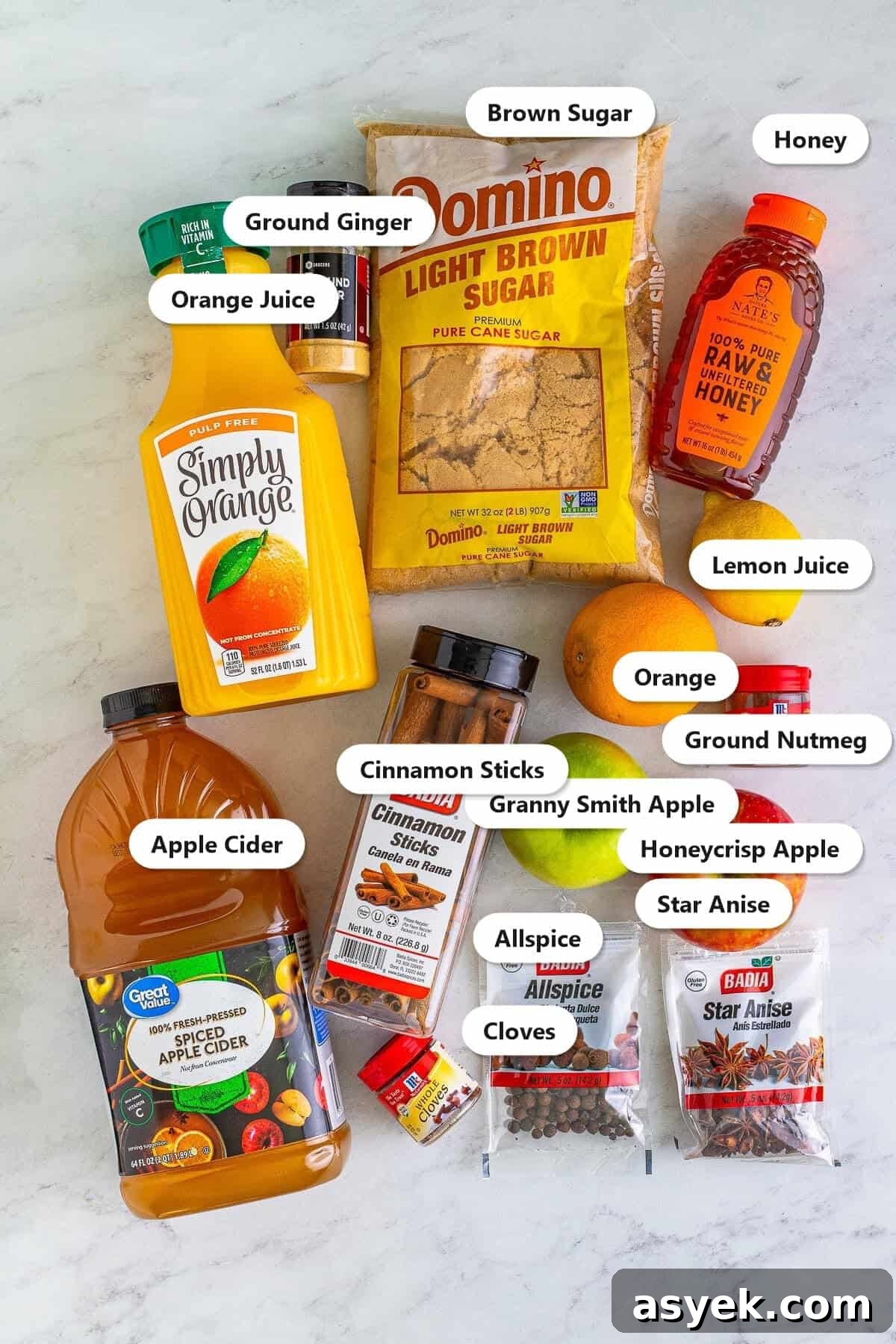 Labeled ingredients to make slow cooker wassail including apple cider, orange juice, brown sugar, honey, and warm spices.