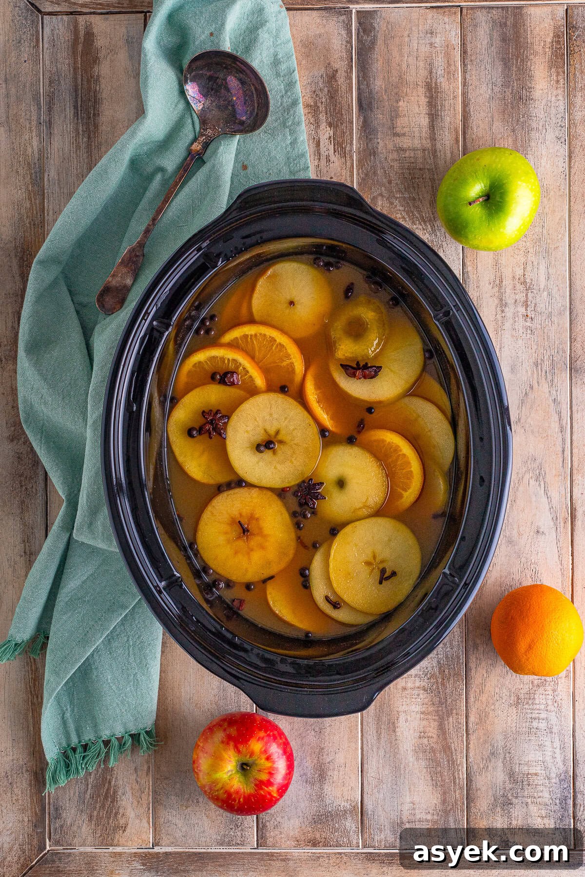 An overhead view of slow cooker wassail filled with floating apple and orange slices.