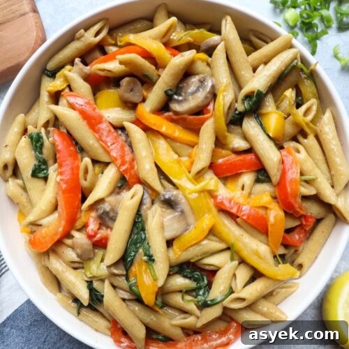 white bowl with creamy jerk pasta with bell peppers, mushrooms, spinach, and green onion.