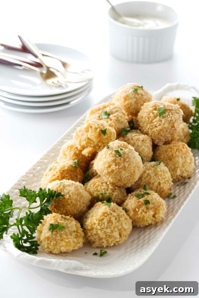 Golden baked balls with parsley on a white platter, dipping sauce behind.