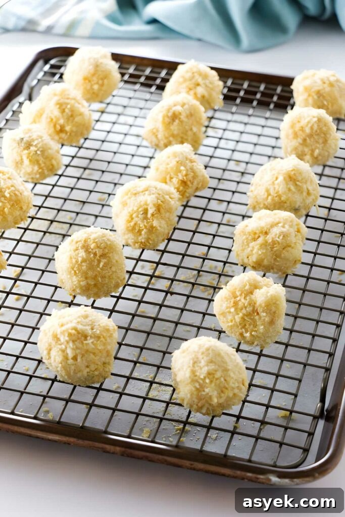 Uncooked coconut-coated dough balls on a cooling rack over baking sheet.