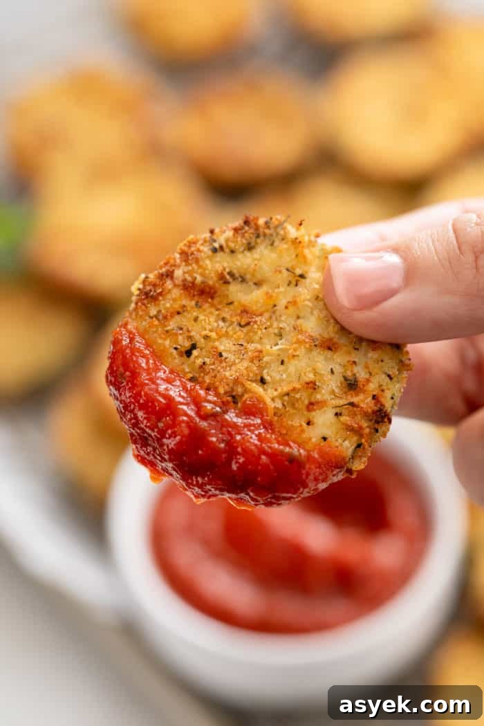 Crispy Air Fryer Zucchini Chips Recipe 11 Hand holding up an air fryer zucchini chip dipped in marinara sauce.