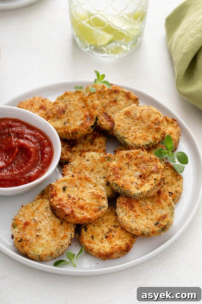 Crispy Air Fryer Zucchini Chips Recipe 3 White plate filled with air fryer zucchini chips and a small bowl of marinara sauce.