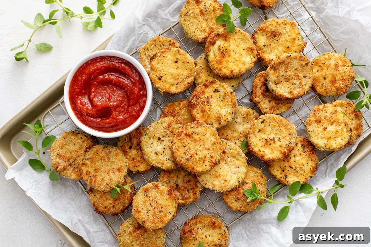 Crispy Air Fryer Zucchini Chips Recipe 10 Air fryer zucchini chips and a bowl of marinara sauce set on a parchment-lined baking sheet.