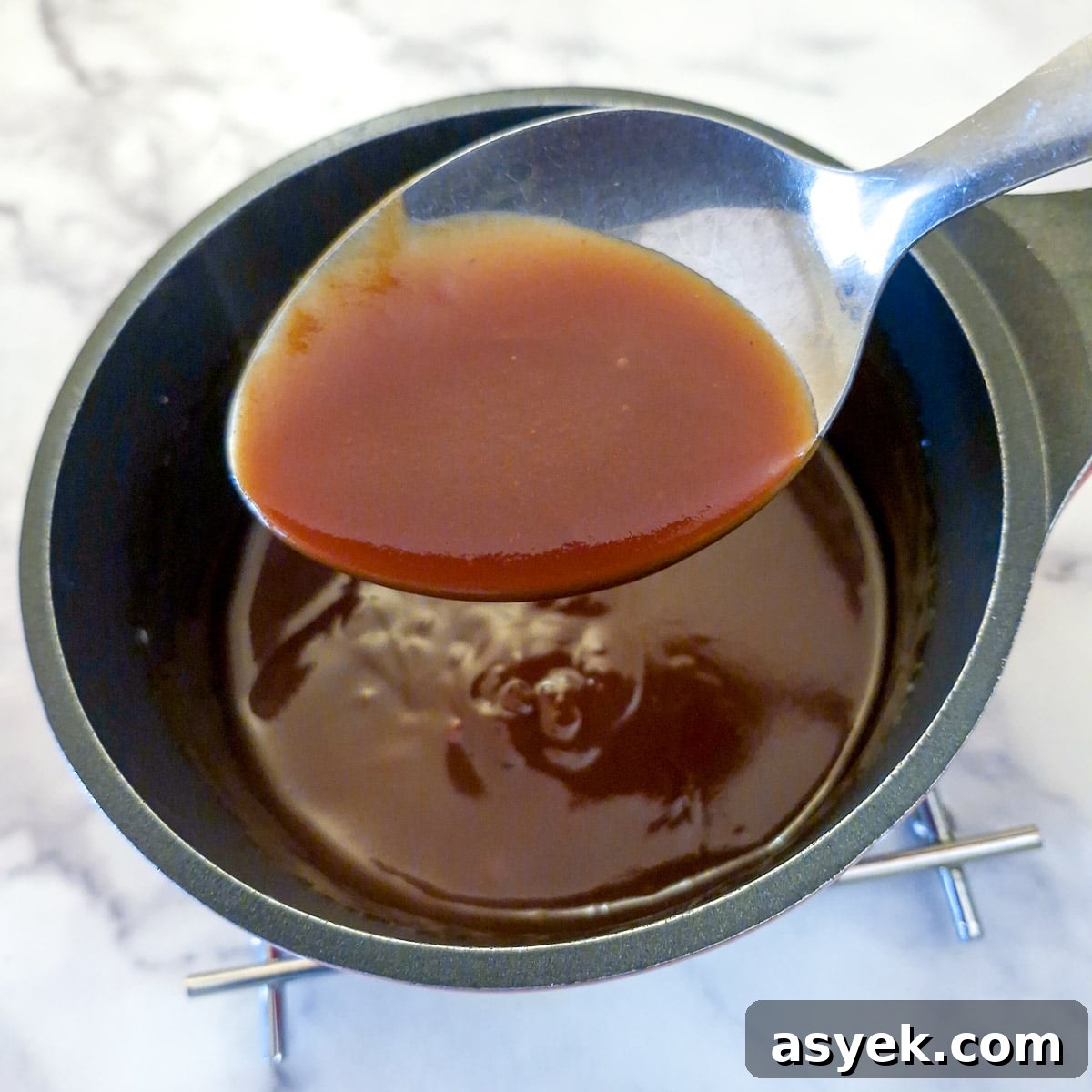 Thickened sweet and sour sauce on a spoon held over the saucepan.