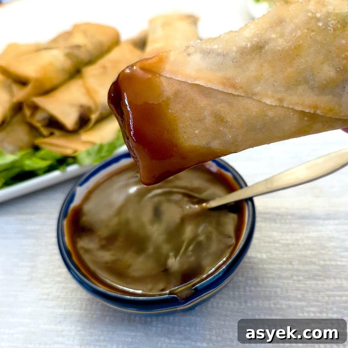A spring roll being dipped into a bowl of sweet and sour dipping sauce.