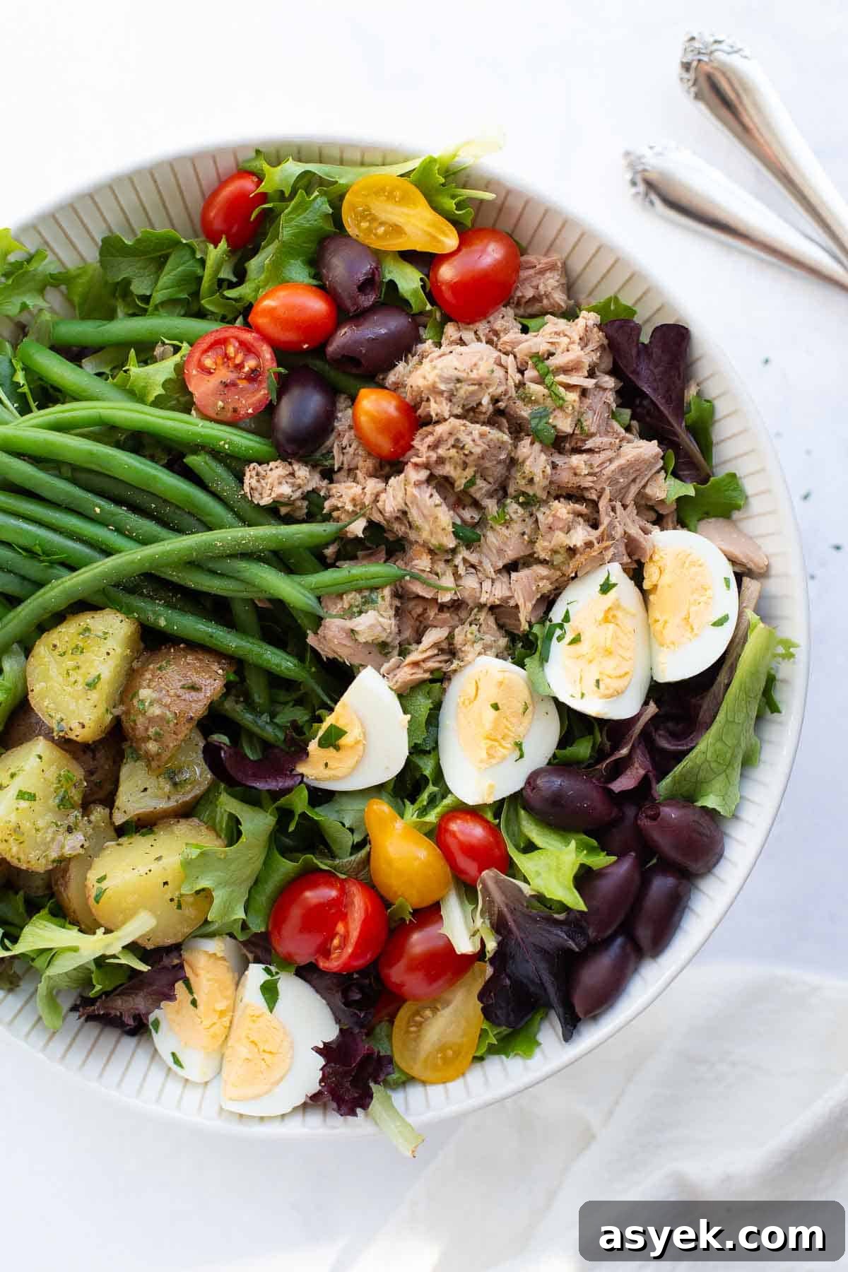 Salad Nicoise Salad niçoise in a bowl with utensils on the counter.