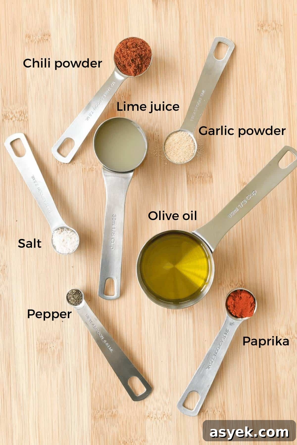 The seasonings for the smoked chili lime chicken measured out and placed in measuring spoons on a wooden table.