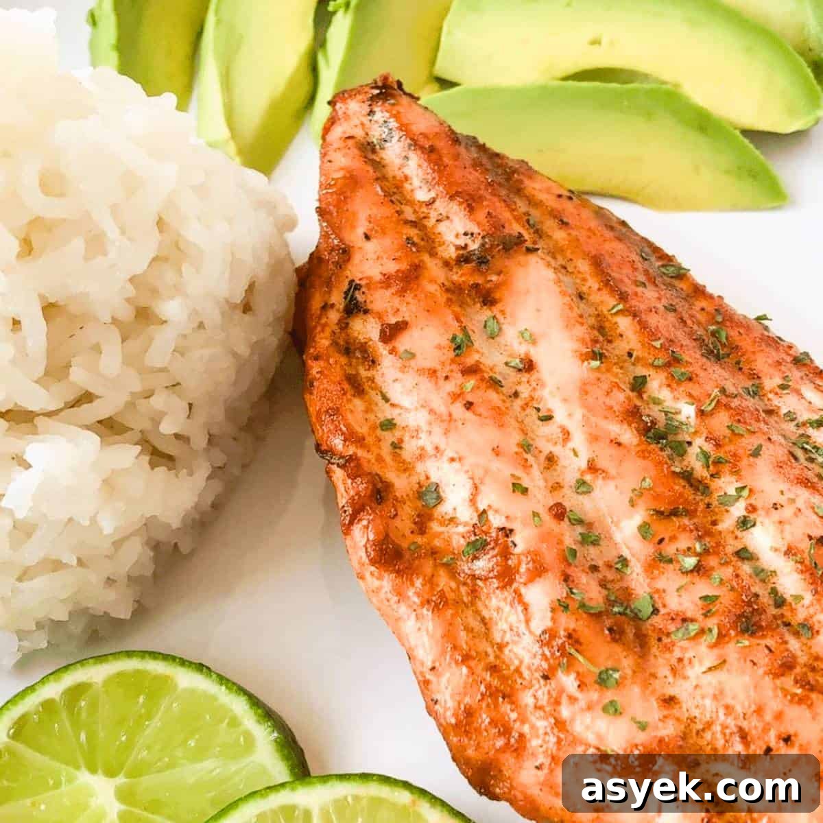 A smoked chili lime chicken breast on a plate with white rice, lime slices, and avocado slices.